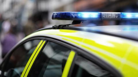 A photo of the roof of a police car with sirens flashing. The background is blurred.