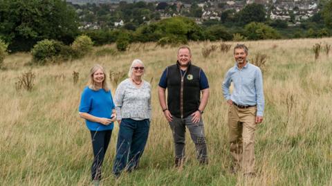 Directors from the Heavens Valley Community Benefit Society pose for the camera as they stand on grass at the Heavens in Stroud. They are joined by current landowner Moreton Cullimore who is also smiling.