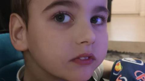 A close up of Jacob, 10, with brown eyes and brown hair sitting on a teal coloured chair.  