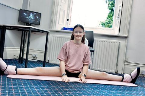 Nadia - wearing a pink top, doing the splits on a pink yoga mat on a blue carpet