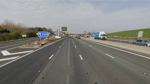 The M1 motorway with a slip road off to the left and a blue sign saying A509. There is not much traffic on the road.