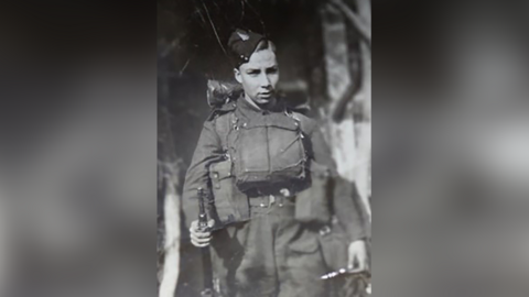 A young boy in army uniform pictured in black and white. 