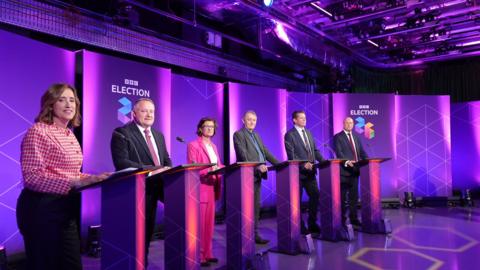 Party leaders standing behind podium all looking at the camera