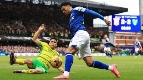 Norwich's Marcelino Nunez is pictured sliding to tackle Dane Scarlett of Ipswich. The scoreboard in the background says 2-2