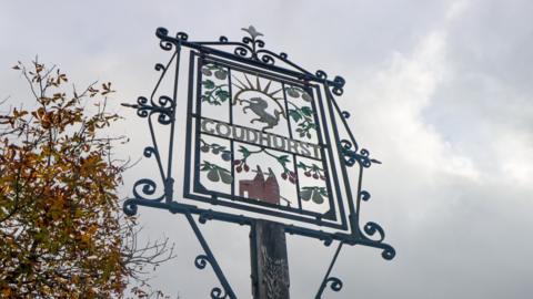 A metal village sign which says "Goudhurst" in the middle.