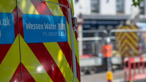 A yellow and red striped van with the Wessex Water logo on it set against a blurred background of a high street.