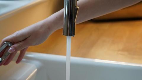 A woman's hand turned on a running tap.