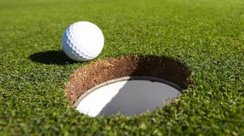 A golf ball teeters on the edge of a hole on a golf green.