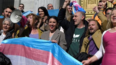A crowd holding a transgender flag and cheering