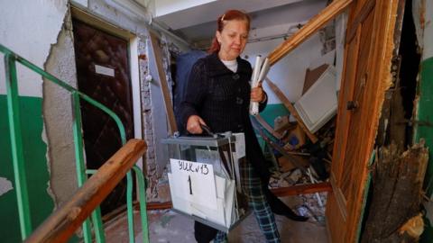 An electoral worker carries a ballot box through a ruined block of flats in Mariupol, 25 September