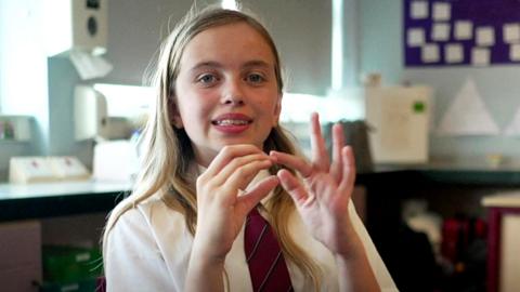 A child uses sign language to say carbon footprint