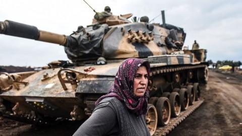 A Turkish villager stands next to Turkish army tanks as soldiers gather close to the Syrian border on 21 January 2018 at Hassa, in Hatay province
