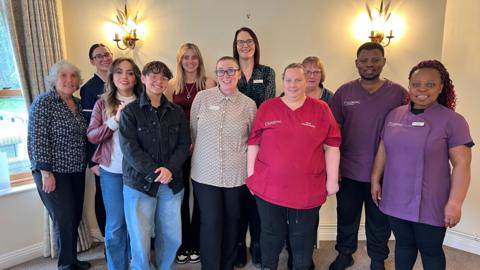 All of the families who work at the home stood together in a well lit room.