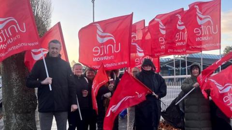 Unite the Union members hold red flags on the picket line at Glenveagh school in south Belfast