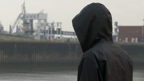 An image showing a person standing with their back to the camera and the hood of their black coat up
