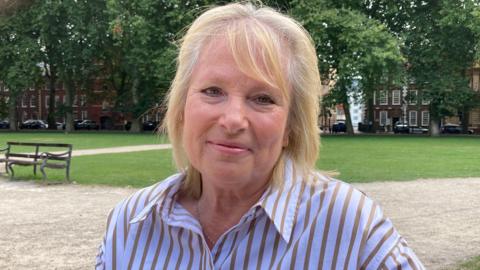 Liz Roberts. She has short blonde hair and is wearing a striped shirt. She is pictured outside. Liz is looking directly at the camera and smiling.