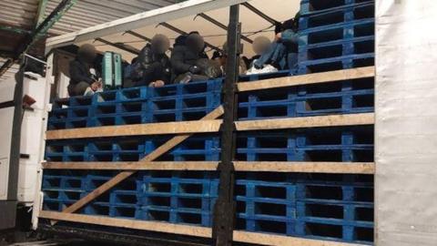 Photo of people being smuggled in the back of a lorry filled with blue pallets, their faces blurred so as to be unrecognisable.