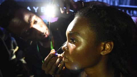 A make-up artist uses a phone's light to prepare a model following an electrical problem during the Lagos Fashion Week - 25 October 2018