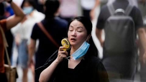 A woman uses a handheld fan while walking along the street in Shanghai