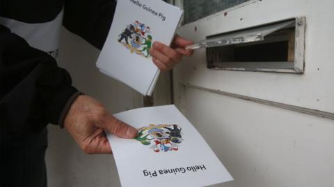 A "Not Our Future" volunteer posts leaflets with the words "Hello Guinea Pig" through a letterbox in Oxford