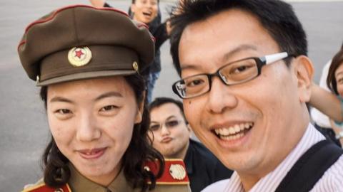 Photo of Aram Pan having North Korean street food in front of a North Korean flag.