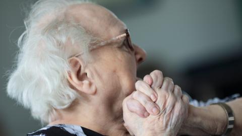 elderly person in a care home clasping hands