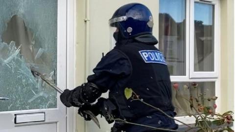 A police officer smashing in a glass panel on a door