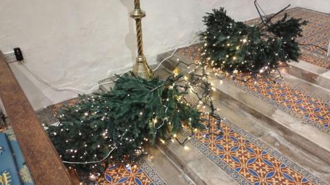 A Christmas tree lies on the the floor of a church after it was targeted by vandals. The yellow lights on the tree remain on