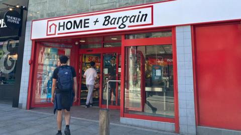 A red and white shop front with black writing which says Home and Bargain. Two men are walking into the shop.