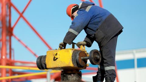 A Worker In Overalls And A Hard Hat Repairs And Maintains A Linear Crane Of The Main Gas Pipeline - in Barnaul Russia