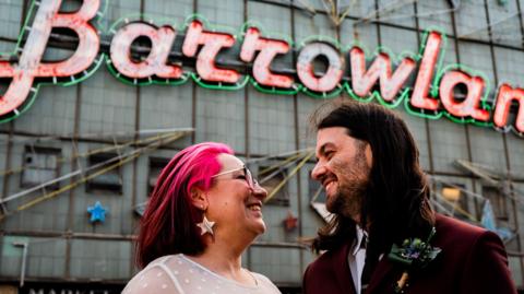 Bride and groom looking at each other, smiling in their wedding outfits standing in front of the Barrowland Ballroom in Glasgow