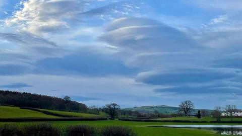 Lenticular clouds in a blue sky with fields which are slightly waterlogged to the right