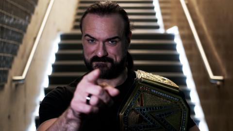 Drew McIntyre - seated and pointing while wearing the WWE title belt over his shoulder