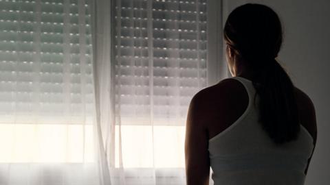 Rear view of an unrecognizable abused woman sitting on her bed looking out the window