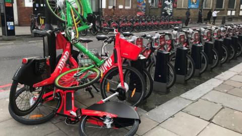 A discarded Lime e-bike thrown on top of other docked e-bikes in London.