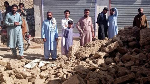 Residents gather near the rubble of a damaged house following an earthquake in Harnai, Balochistan, Pakistan, on 7 October 2021