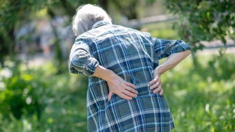 Woman experiencing back pain in a garden - stock photo