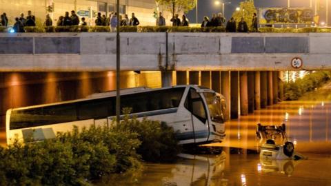 People look on a bus and cars submerged in a flooded road, in Mandra, near Athens