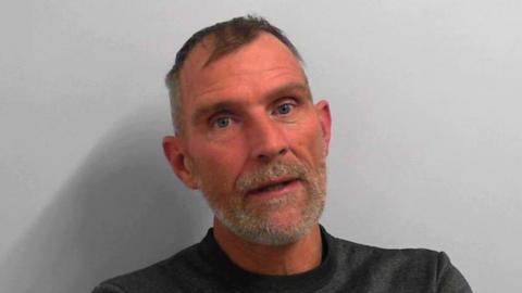 A custody picture of a man with short hair and a grey beard.