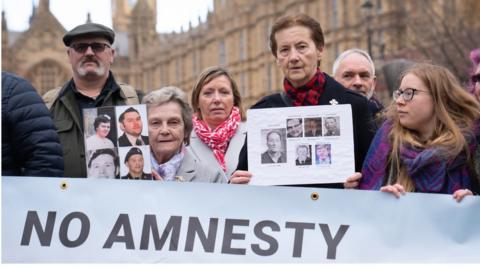 Demonstrators holding photos of their loved ones and a banner that says No Amnesty