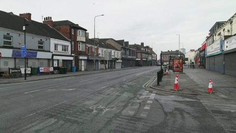 A view of the scene, with traffic cones on the side of the road by a junction.