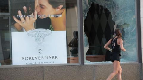 A jogger runs past a broken Chicago storefront window after parts of the city had widespread looting and vandalism, on August 10