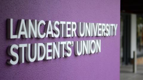 The Lancaster University Students' Union logo in white on a purple wall