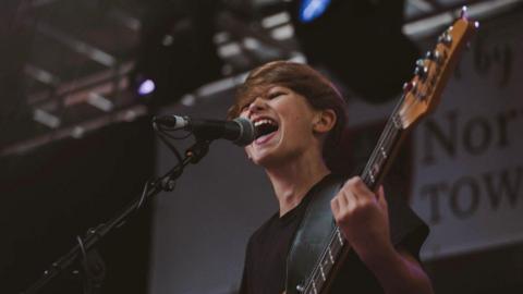 Teenage boy singing and playing guitar on stage