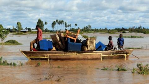 Residents use a boat to carry their belongings through the waters after their homes were flooded as the River Nzoia burst its banks