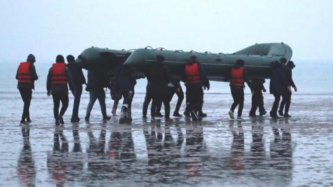 A group of more than 40 migrants run on the beach with an inflatable dinghy, as they leave the coast of northern France, on 24 November 2021