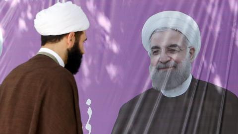 An Iranian cleric walks near an election poster of Iranian President Hassan Rouhani in front of his campaigning office in the city of Karaj, Albroz province, Iran, 28 April 2017