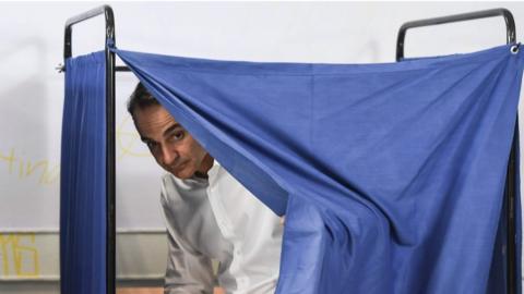 Kyriakos Mitsotakis peeks out from behind the blue curtain of a polling booth