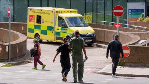 A yellow ambulance with the words Emergency Ambulance parked outside a hospital emergency department 