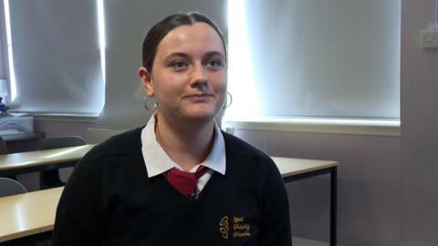 Eilidh, sgoilear aig Sgoil Ghàidhlig Ghlaschu agus i na suidhe sa chlas. 
